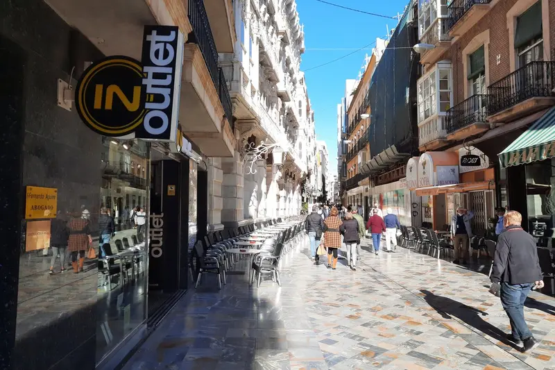 Gente paseando al sol por la Calle Mayor de Cartagena, con su suelo de mármol, terrazas y miradores modernistas.